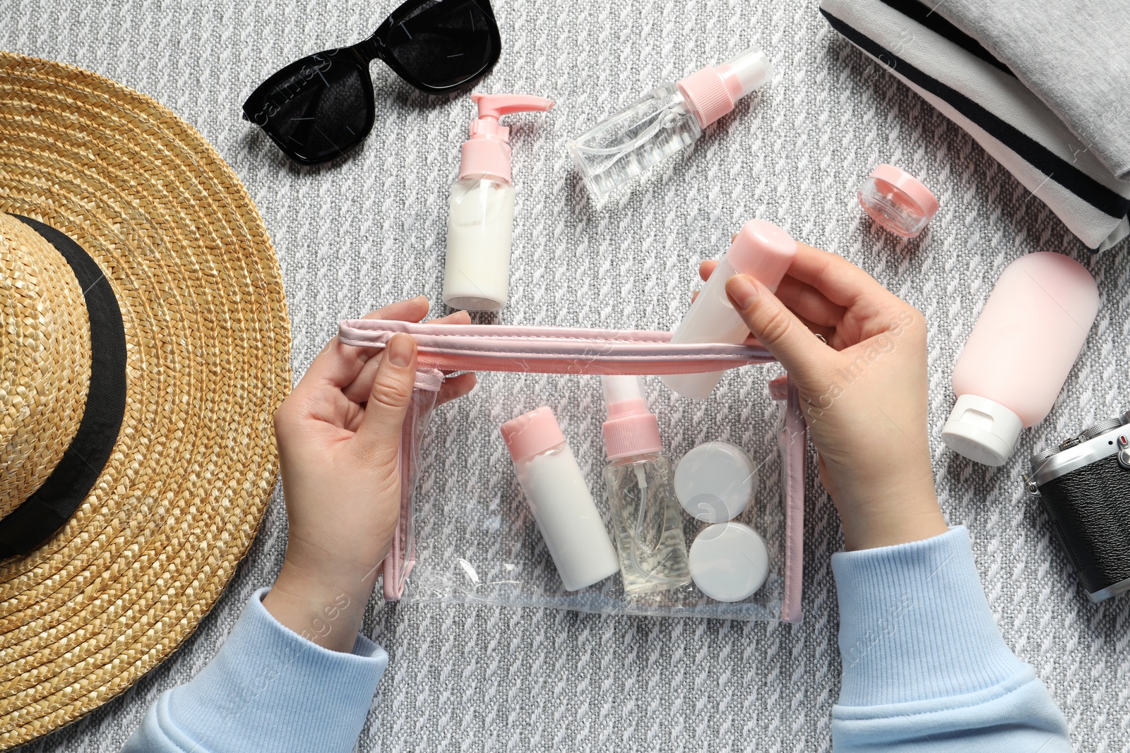 Photo of Cosmetic travel kit. Woman putting small bottle with personal care product into plastic bag on sofa, top view