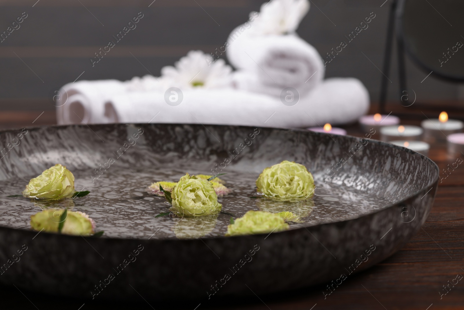 Photo of Bowl of water with flowers on wooden table, closeup. Pedicure procedure