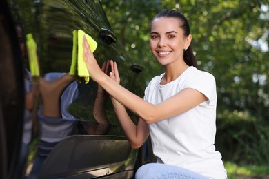 Photo of Happy woman washing car door with rag outdoors