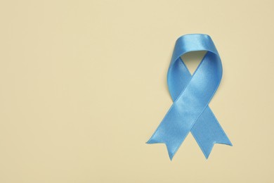 Light blue awareness ribbon on beige background, top view. Space for text