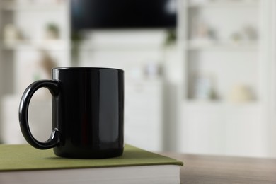 Photo of Blank ceramic mug and book on wooden table. Mockup for design