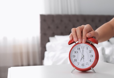 Woman turning off alarm clock on table in bedroom. Time to wake up