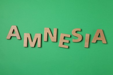 Photo of Word Amnesia made of wooden letters on green background, flat lay