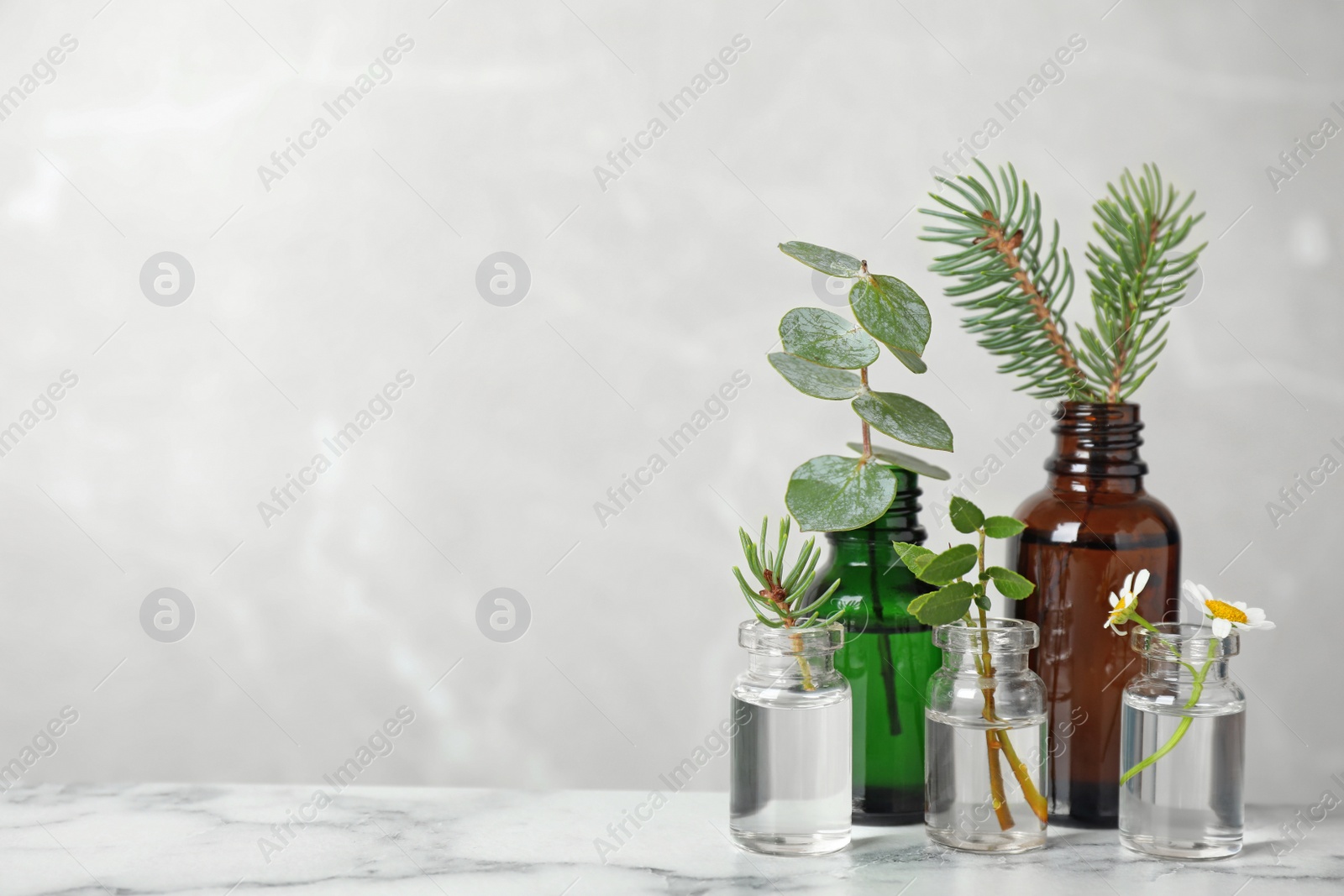 Photo of Glass bottles of different essential oils with plants on table. Space for text