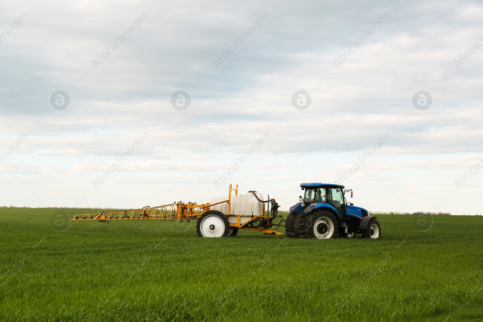 Photo of Tractor spraying pesticide in field on spring day. Agricultural industry