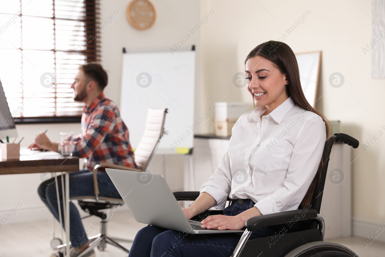 Photo of Portrait of woman in wheelchair with laptop and her colleague at workplace