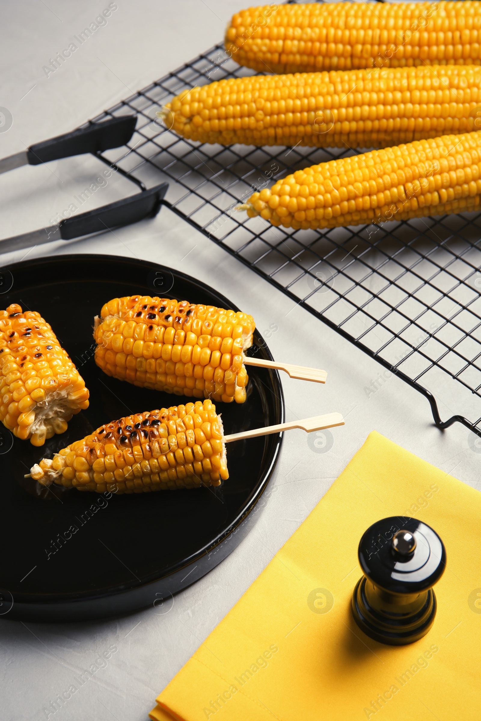 Photo of Ceramic plate with grilled corn cobs on light background