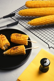 Ceramic plate with grilled corn cobs on light background