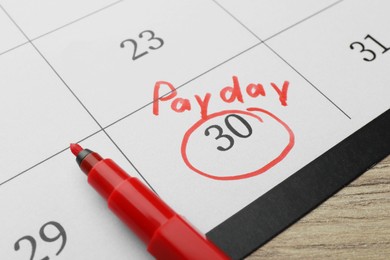 Photo of Calendar page with marked payday date and red marker on table, closeup