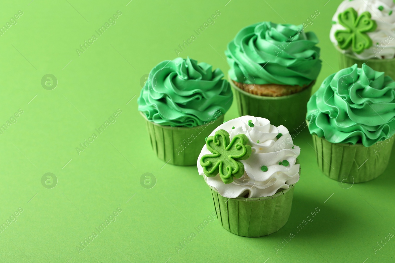 Photo of St. Patrick's day party. Tasty festively decorated cupcakes on green background, closeup. Space for text
