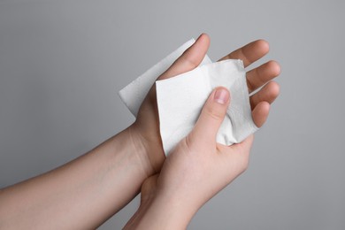 Woman wiping hands with paper towel on grey background, closeup