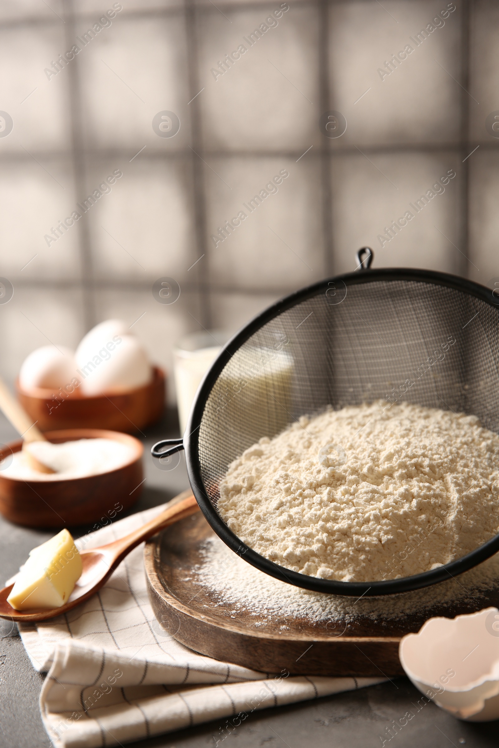 Photo of Making dough. Flour in sieve, spoon and butter on grey table, closeup