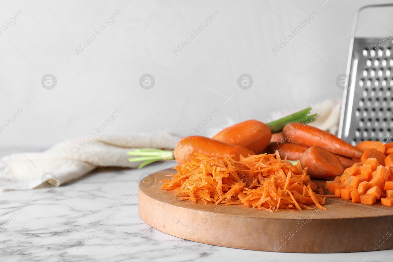 Photo of Board with differently cut carrots on marble table. Space for text