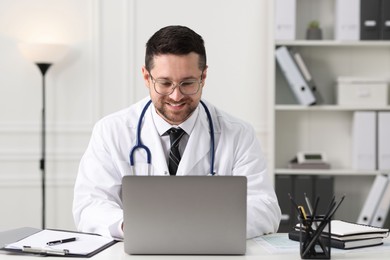 Photo of Smiling doctor having online consultation via laptop at table in clinic