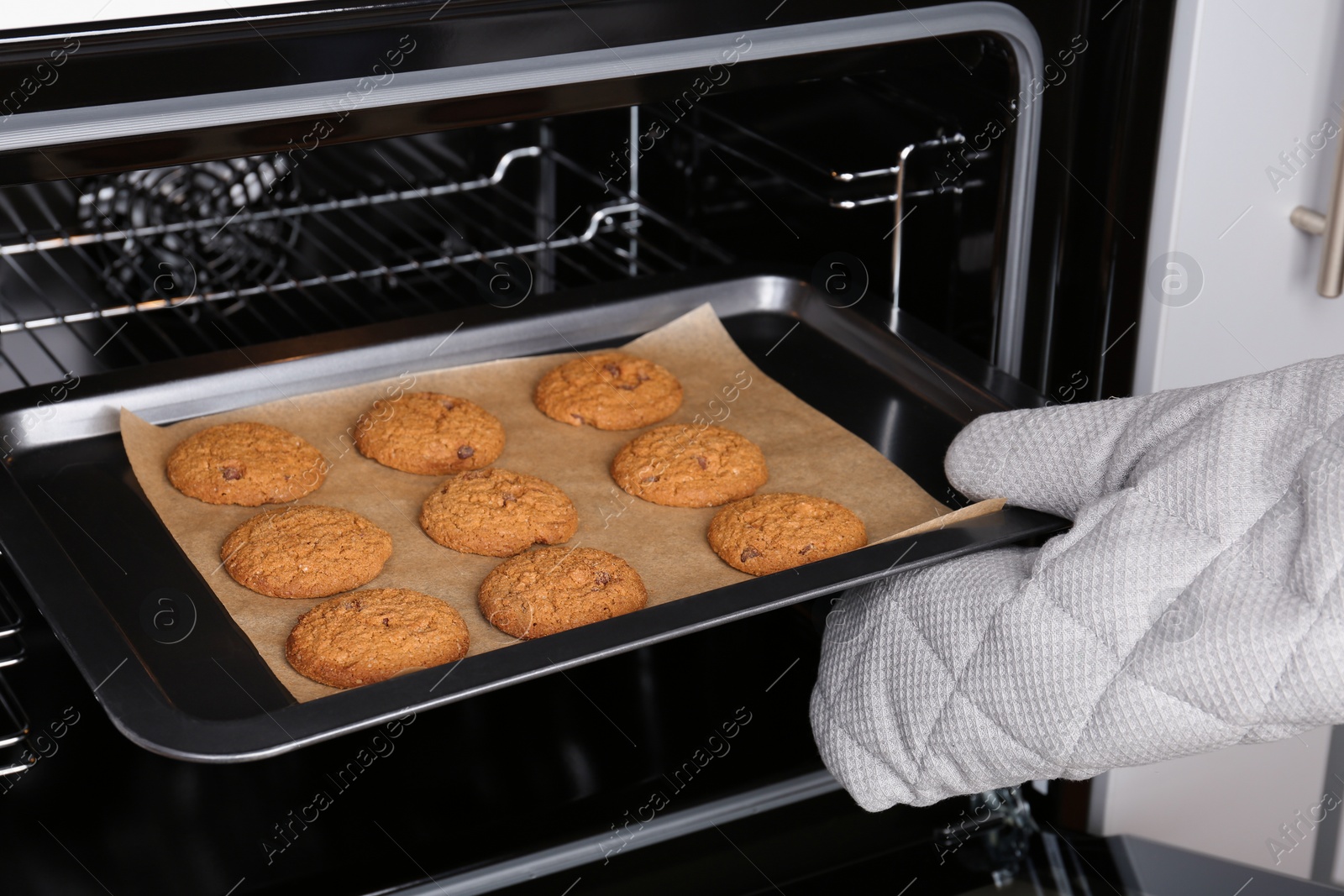 Photo of Woman taking baking tray with delicious cookies out of electric oven, closeup