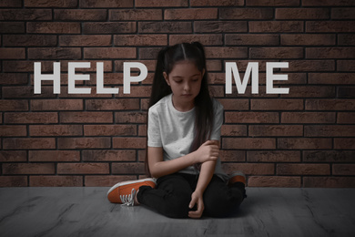 Image of Sad little girl near brick wall and text HELP ME