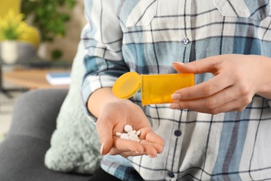 Photo of Woman pouring pills from bottle into hand indoors, closeup