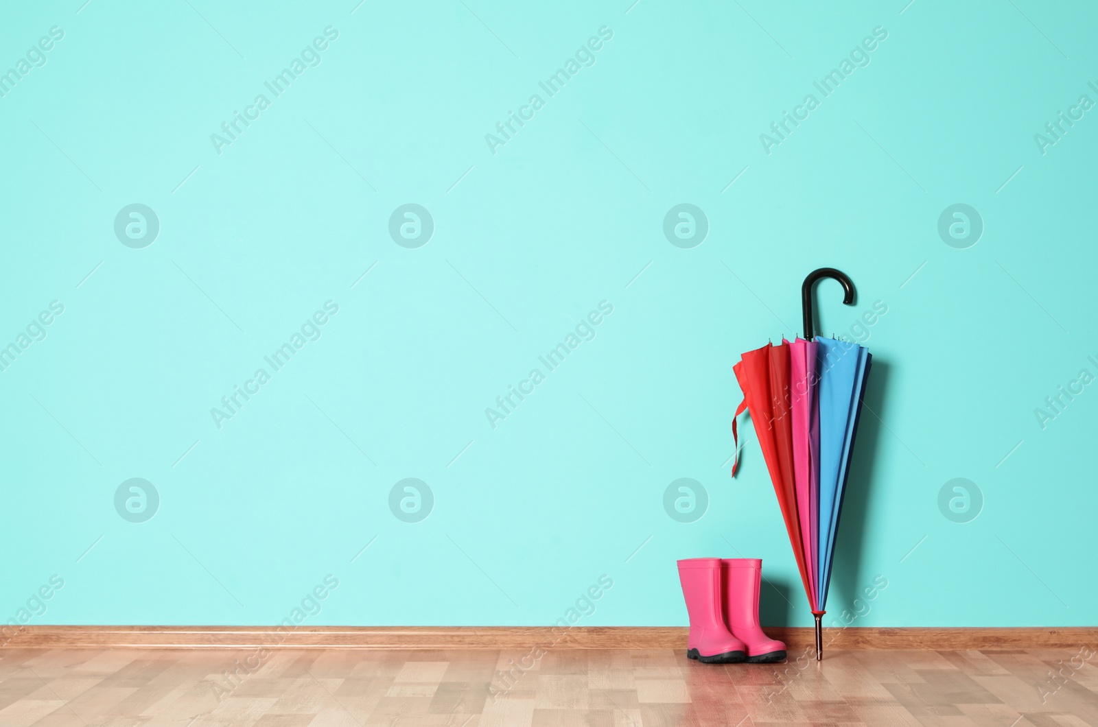 Photo of Umbrella and rain boots on floor near color wall with space for design