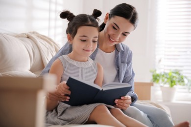Photo of Little girl with mother reading fairy tale in living room