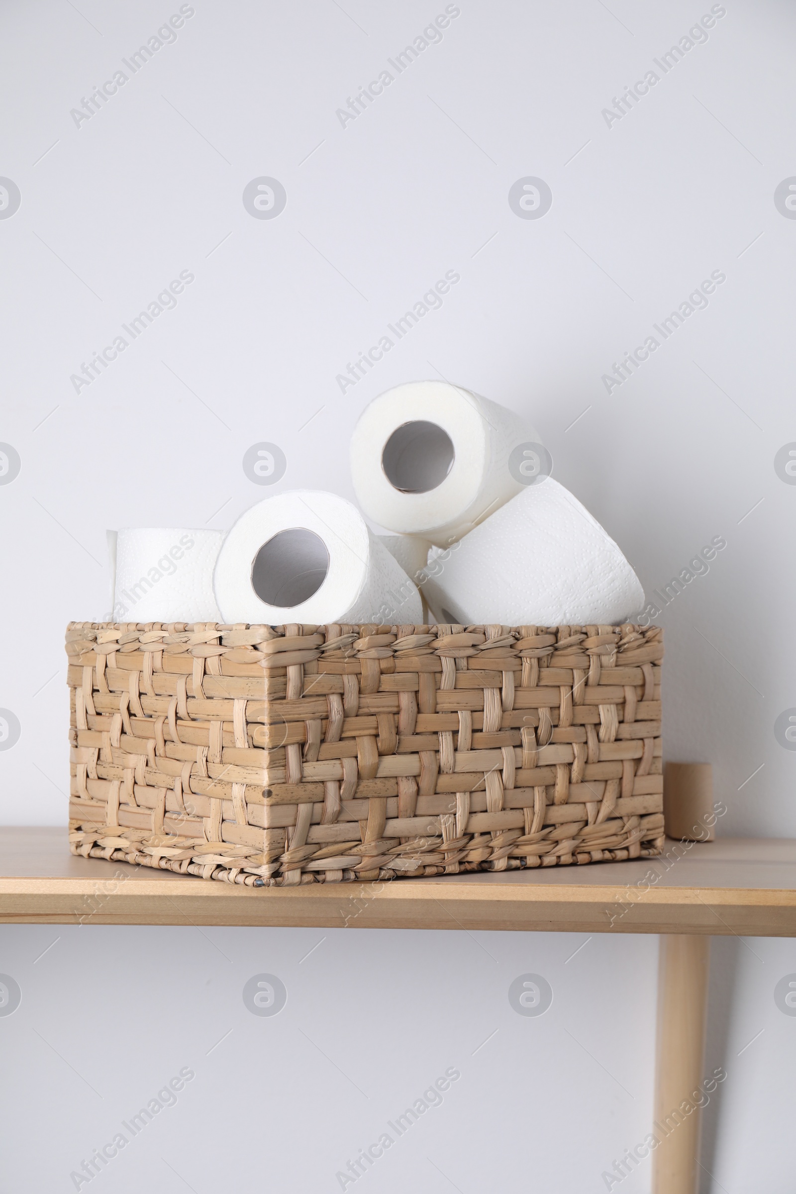 Photo of Toilet paper rolls in wicker basket on wooden table near white wall