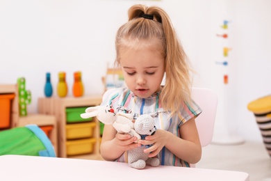 Cute child playing with knitted toys at table in room