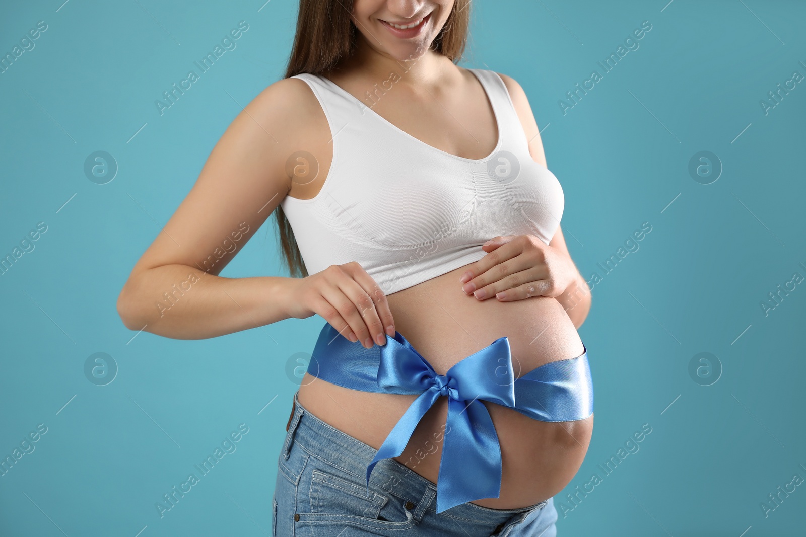 Photo of Young pregnant woman with bow on her belly against light blue background, closeup. Time to give birth
