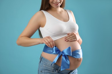 Young pregnant woman with bow on her belly against light blue background, closeup. Time to give birth