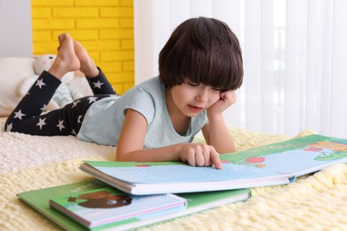 Photo of Cute little boy reading book on bed at home