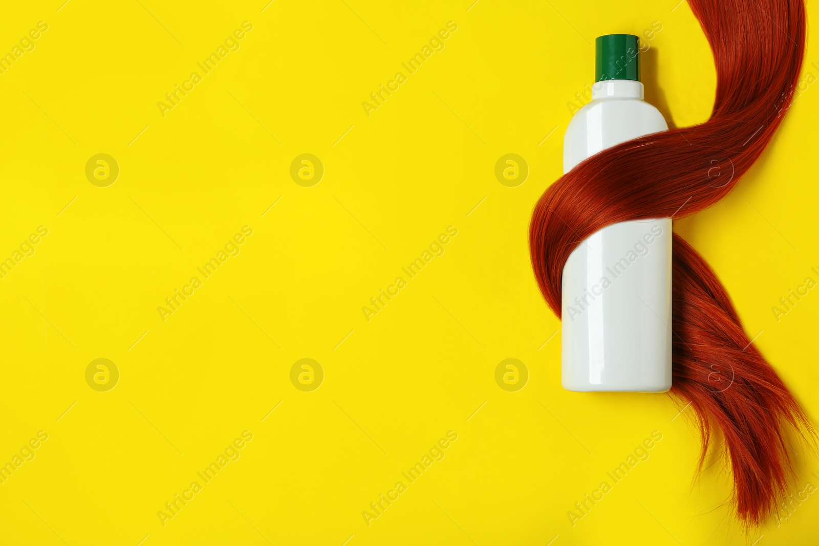 Photo of Shampoo bottle wrapped in lock of hair on yellow background, flat lay with space for text. Natural cosmetic products