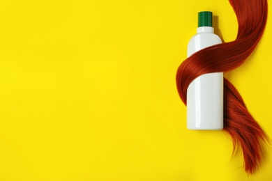 Shampoo bottle wrapped in lock of hair on yellow background, flat lay with space for text. Natural cosmetic products