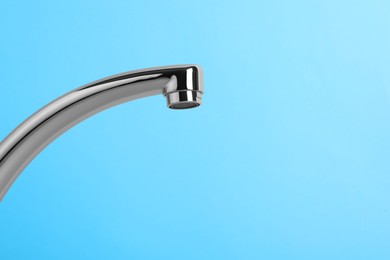 Photo of Modern water tap on light blue background, closeup. Space for text