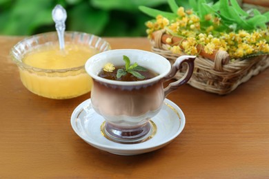 Photo of Cup of hot aromatic herbal tea, honey and linden blossoms on wooden table