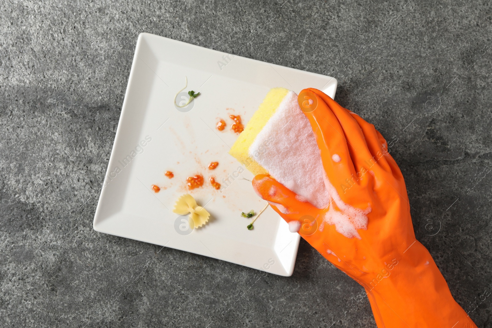 Photo of Woman washing dirty plate at grey table, top view