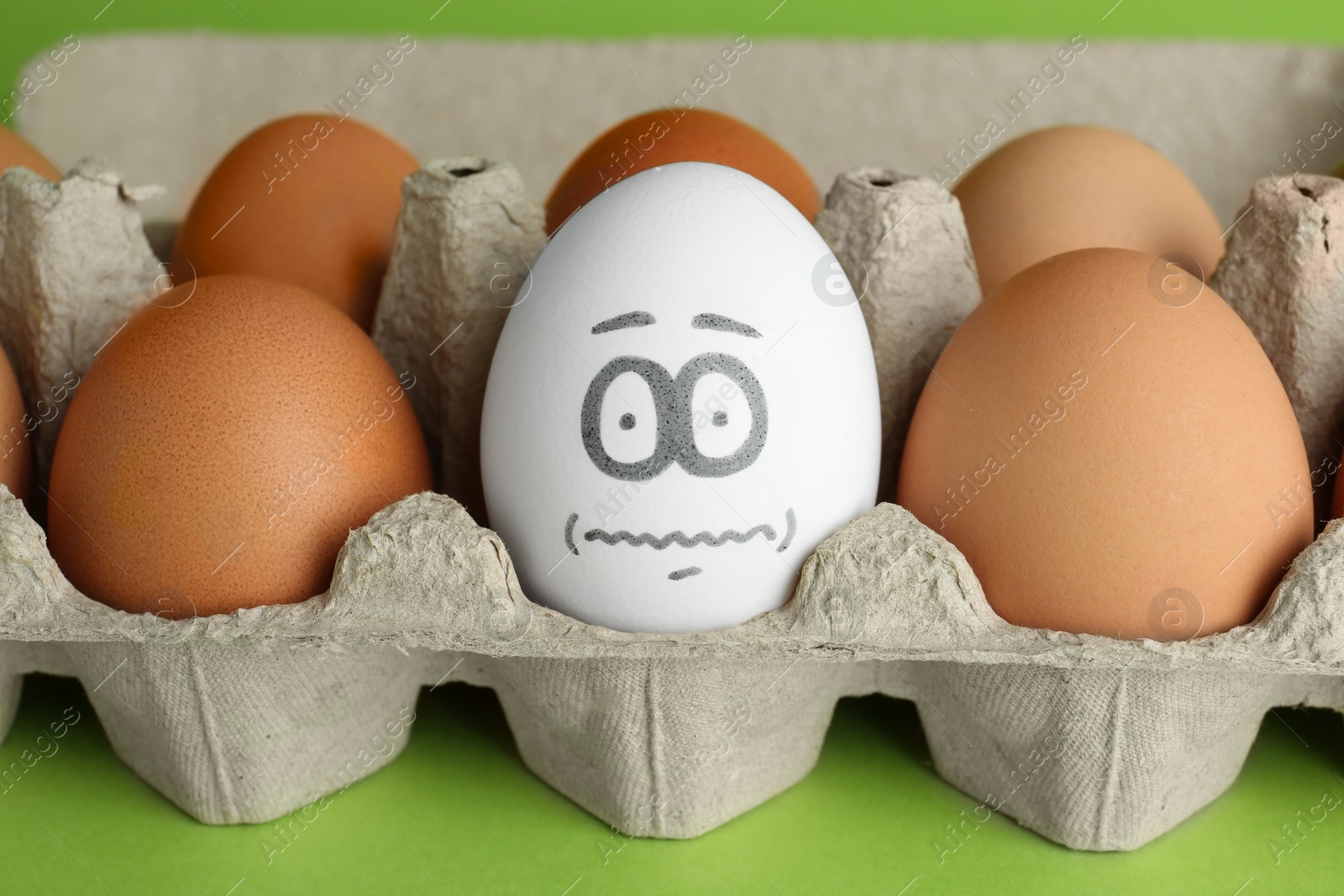 Photo of Egg with drawn frightened face among others in cardboard package, closeup