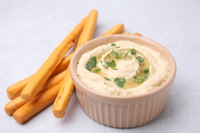 Photo of Delicious hummus with grissini sticks on light grey table