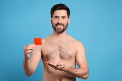 Naked man holding condom on light blue background. Safe sex