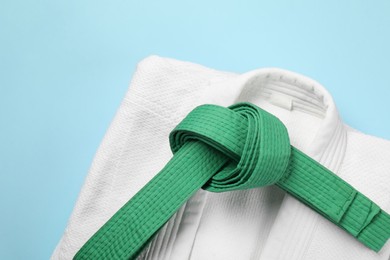 Photo of Green karate belt and white kimono on light blue background, top view