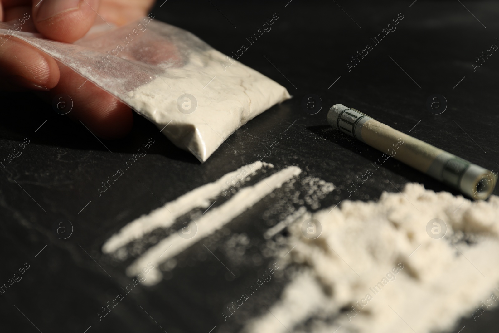 Photo of Drug addiction. Man with cocaine and rolled dollar banknote at dark textured table, selective focus