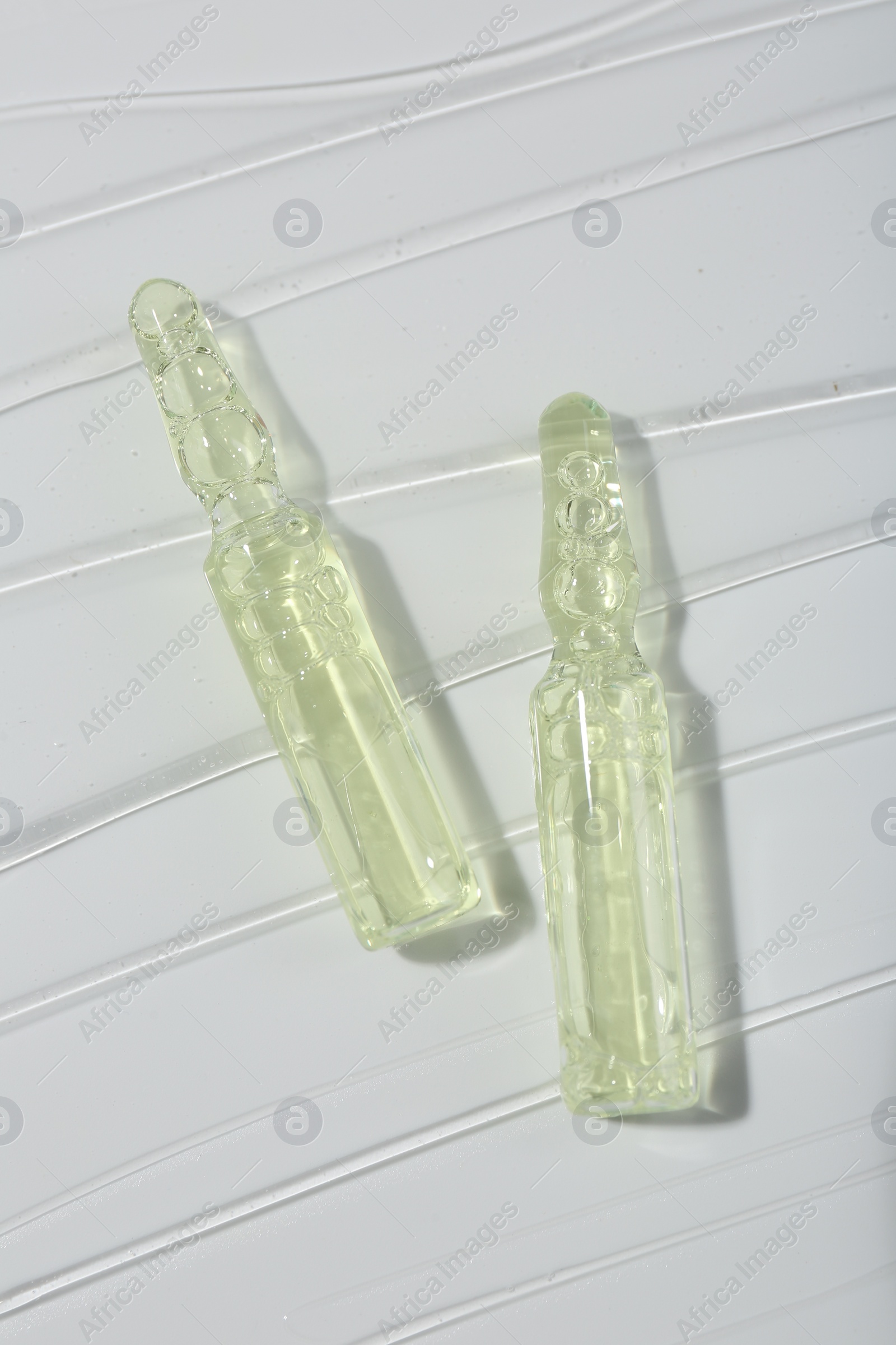 Photo of Skincare ampoules on white surface covered with gel, top view