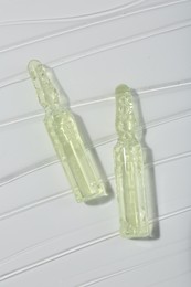 Photo of Skincare ampoules on white surface covered with gel, top view