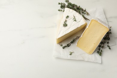 Photo of Pieces of tasty camembert cheese and thyme on white table, top view. Space for text