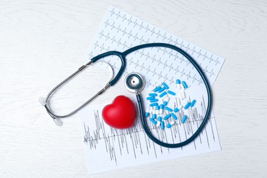 Photo of Stethoscope, heart, pills and cardiograms on wooden background, top view. Cardiology concept