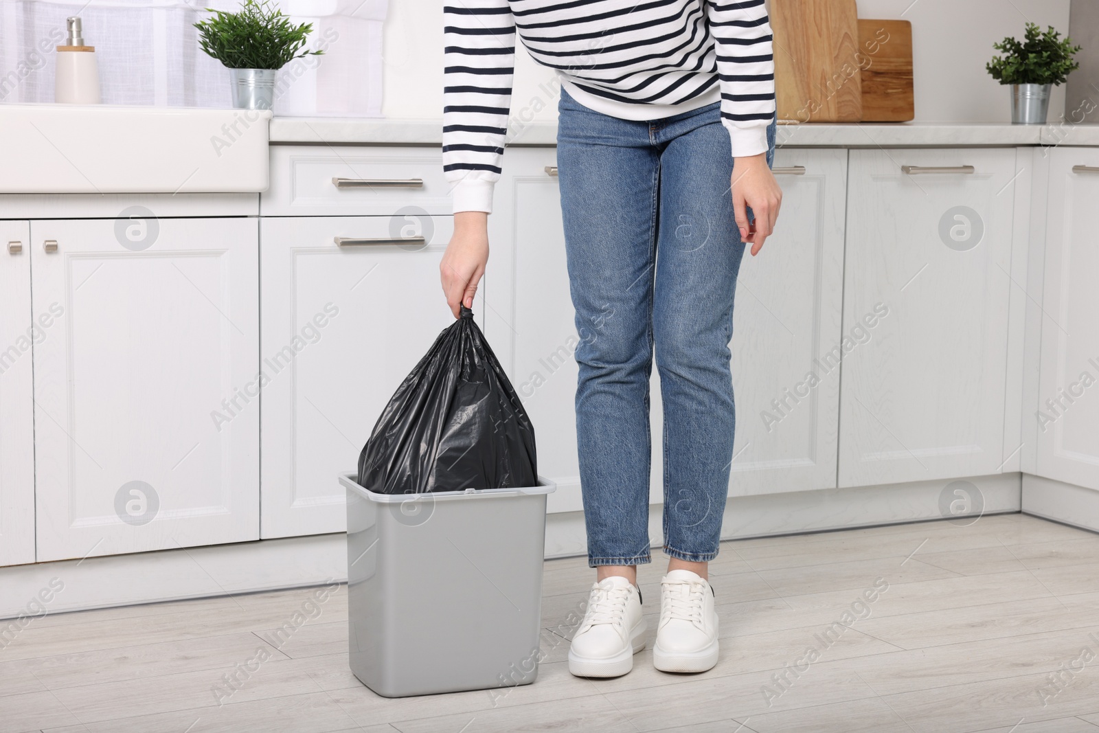 Photo of Woman taking garbage bag out of trash bin in kitchen, closeup