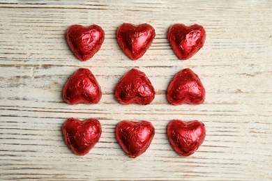 Photo of Heart shaped chocolate candies on white wooden table, flat lay. Valentine's day treat