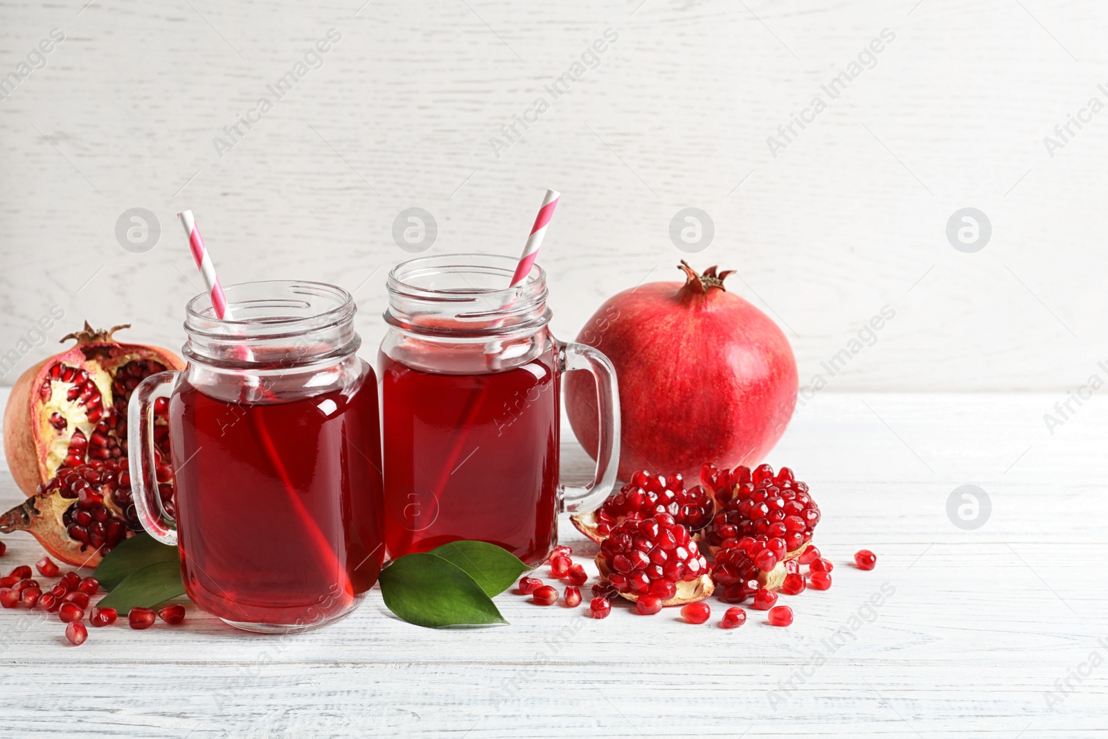 Photo of Mason jars of pomegranate juice and fresh fruits on wooden table, space for text