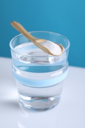 Glass of water and spoon with baking soda on color background