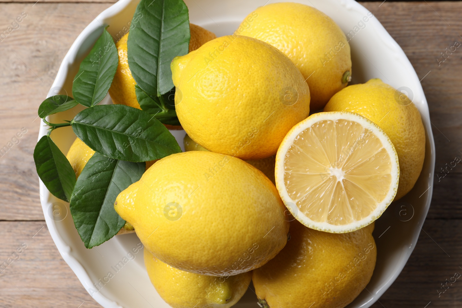 Photo of Fresh lemons and green leaves on wooden table, top view