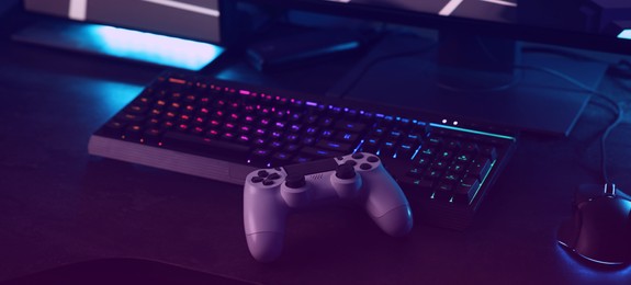 Playing video games. Computer monitor, keyboard, mouse and wireless controller on table indoors