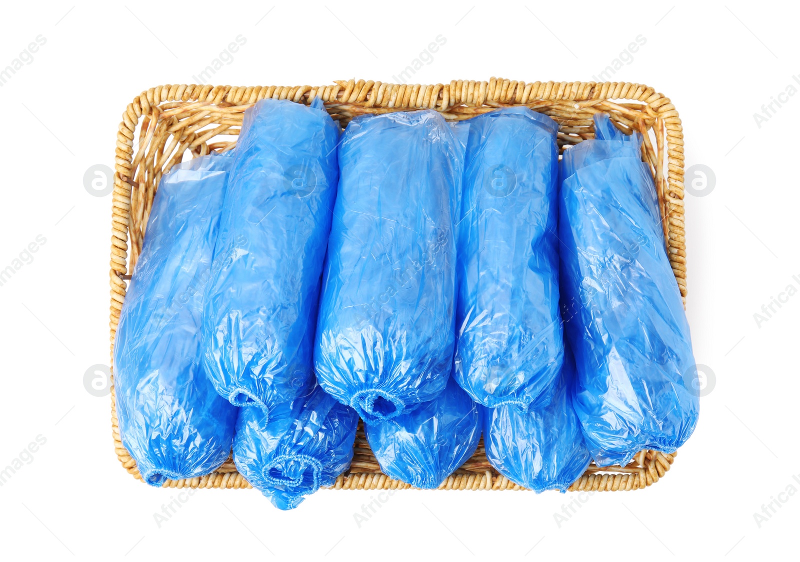 Photo of Rolled blue shoe covers in wicker basket isolated on white, top view