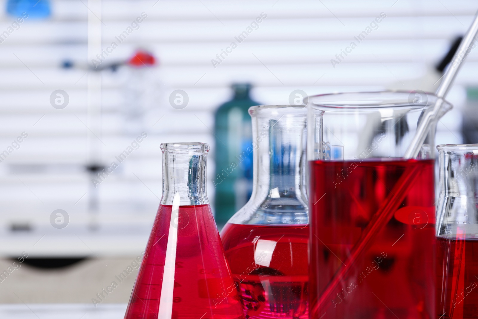 Photo of Laboratory analysis. Different glassware with red liquid on table indoors, closeup. Space for text